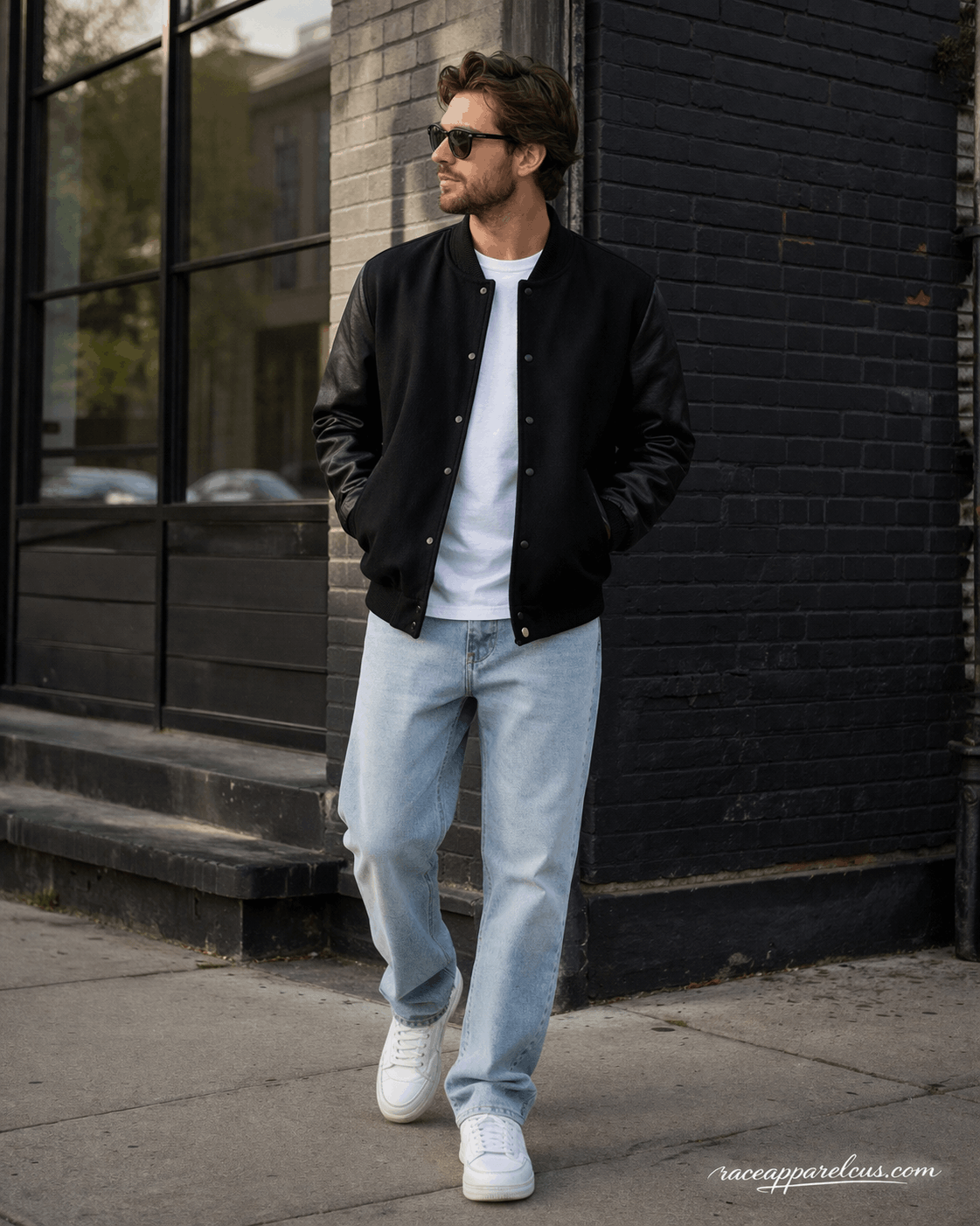 Man wearing all-black varsity jacket with white tee and light wash jeans in urban street setting