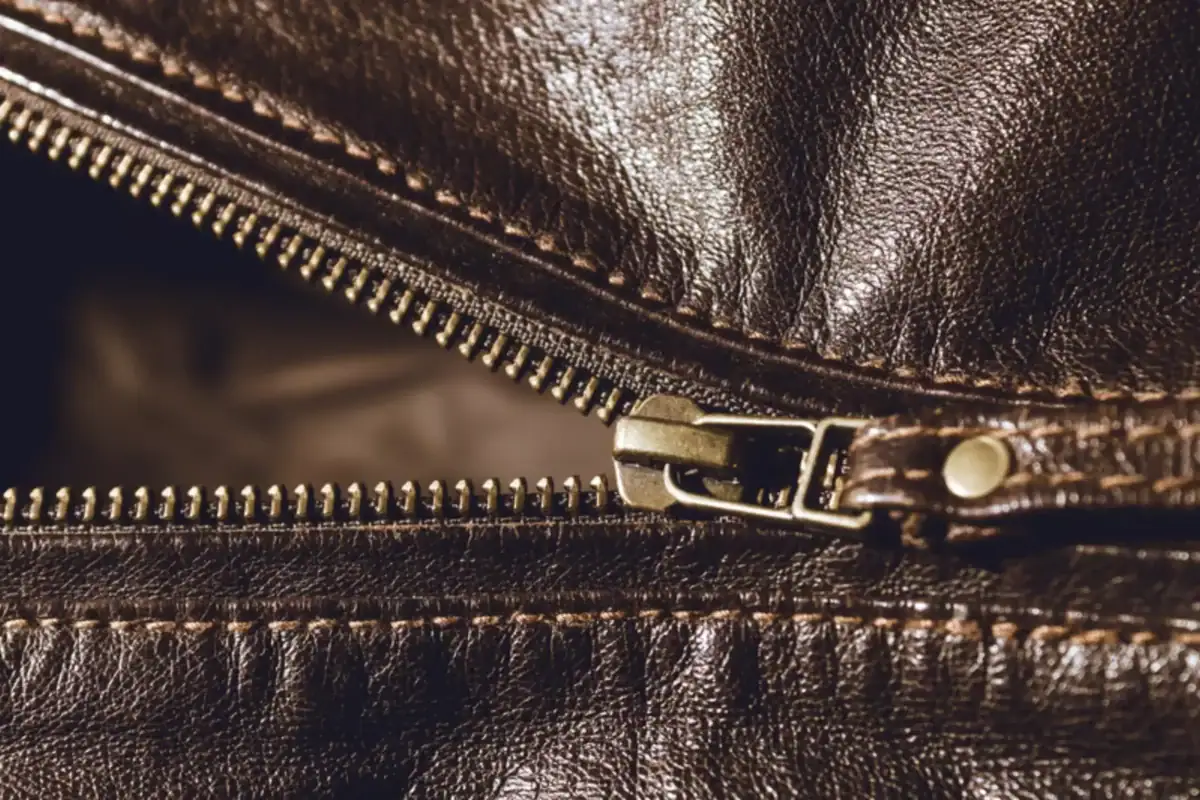 Factory worker inspecting stitching and zipper quality on a leather jacket